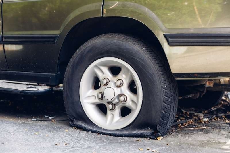 Flat car tire pressed against the ground, indicating a deflated or punctured wheel.