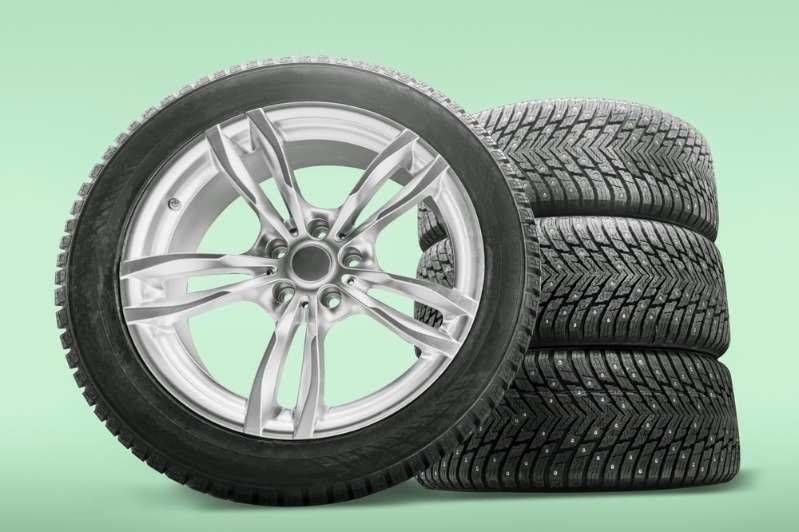 Stack of car tires with alloy wheels displayed against a light green background.