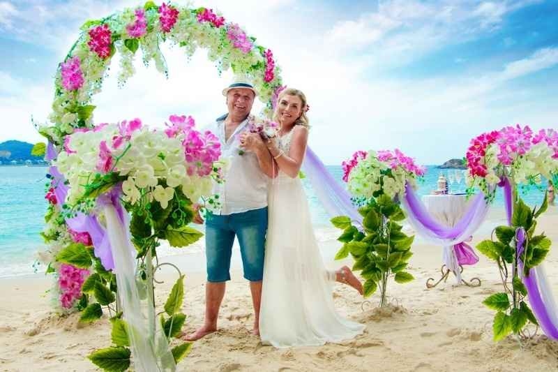Couple posing under a floral arch at a tropical beach wedding.