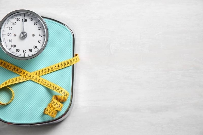 Scale tied with measuring tape on light wooden background, top view.