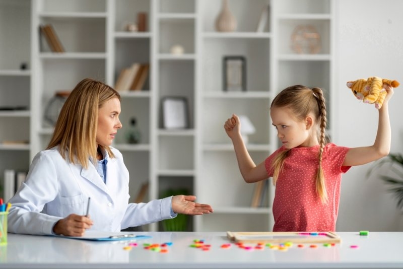 Female healthcare professional speaking with a young girl displaying aggressive behavior during an activity session.