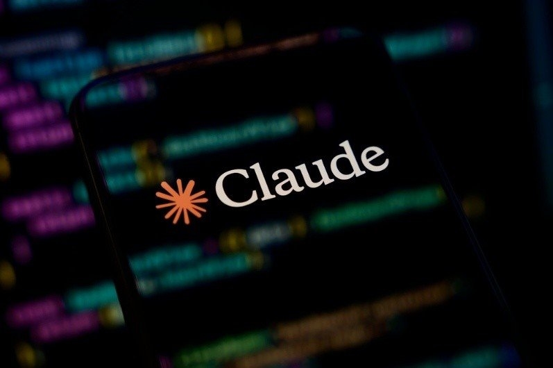 Smartphone displaying the Claude AI logo against a blurred coding background.