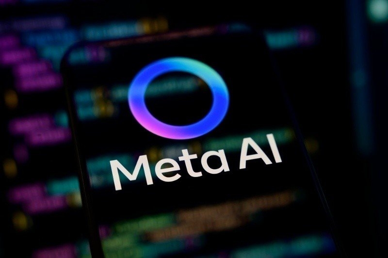 Close-up of a smartphone displaying the Meta AI logo on screen against a blurred background of colorful code and technology graphics.