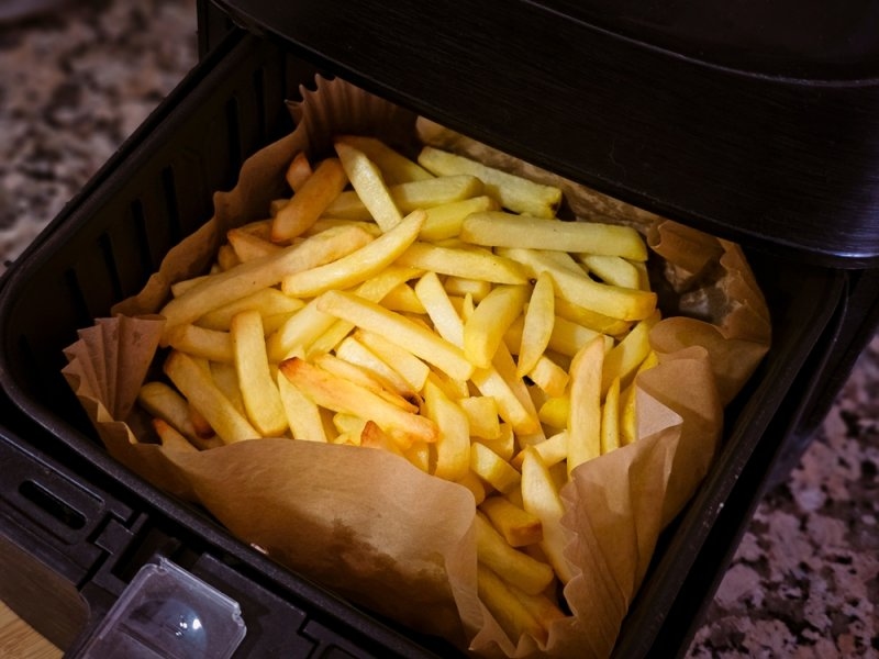 Air fryer with homemade grilled potatoes and greaseproof paper. French fries on air fryer.