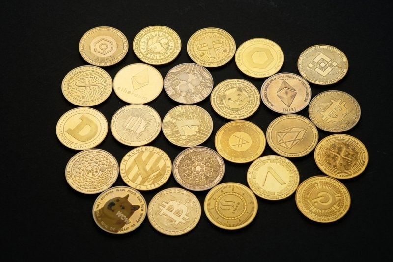 Collection of gold-colored cryptocurrency coins representing various altcoins arranged on a black background.