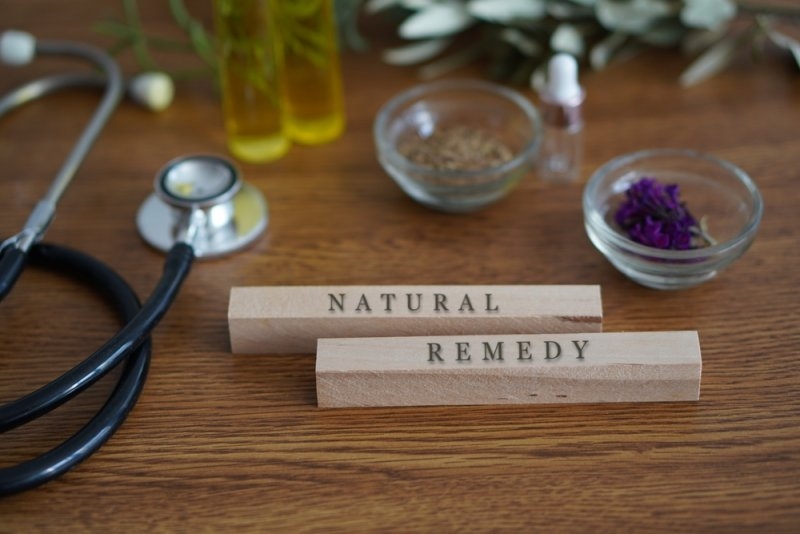 words NATURAL REMEDY written on wooden blocks on a table with plants, herbs, natural oils and a stethoscope.