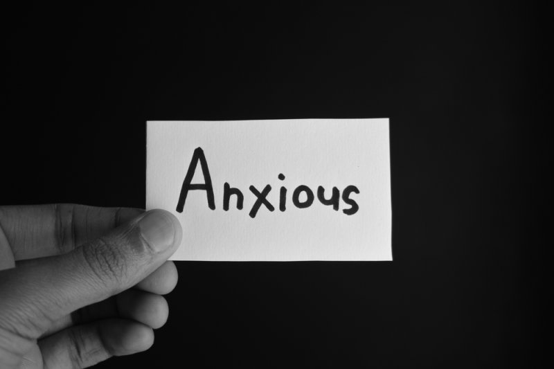 Hand holding a card labeled “Anxious” against a dark background.