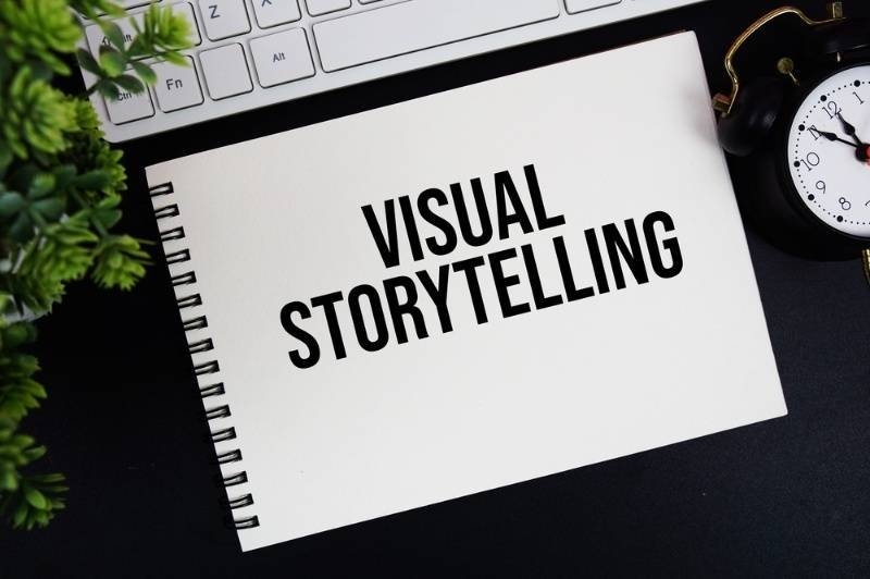 Notebook on a desk displaying the words "Visual Storytelling," surrounded by a keyboard, clock, and plant, representing content creation and creative communication.