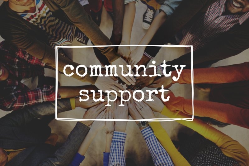 A diverse group of people joining hands around a “Community Support” message.