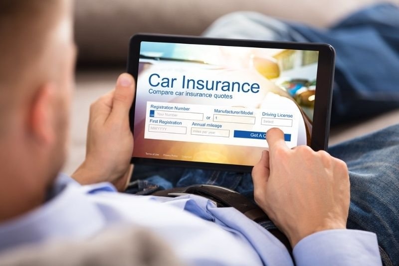 Person using a tablet to compare car insurance quotes by entering vehicle and driver information into an online insurance comparison form