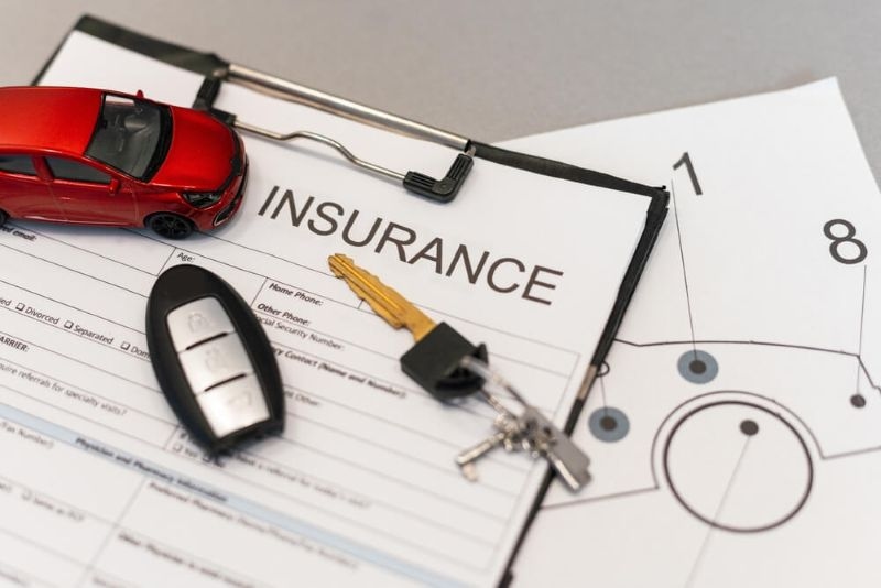 Car insurance papers cliiped to a board with car keys and toy car