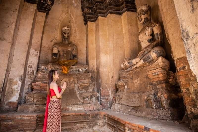 Woman standing with hands together in prayer before historic Buddha statues inside an ancient temple.