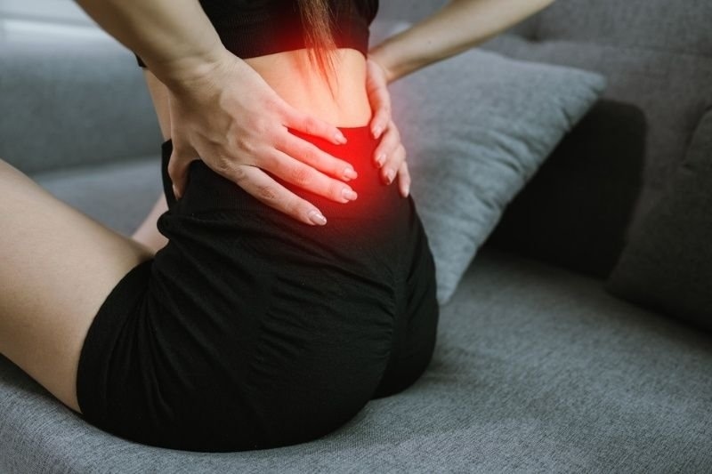 Person holding their lower back with a highlighted red pain area, illustrating back pain or muscle strain.