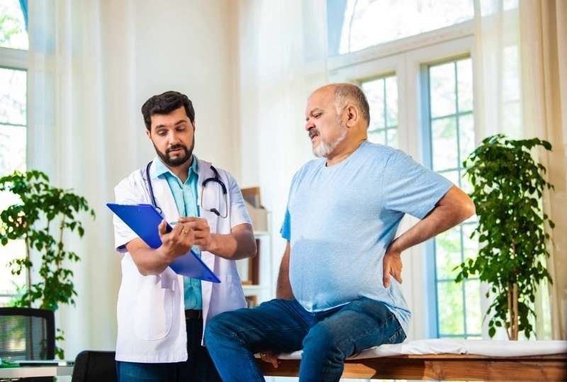 Doctor consulting with an older man experiencing lower back pain during a medical appointment.