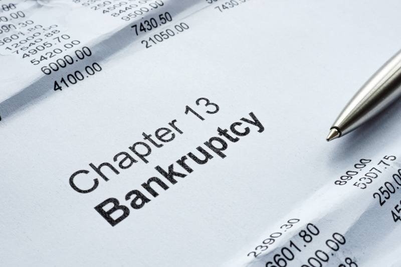 A financial document prominently displays the words “Chapter 13 Bankruptcy,” with a pen and financial figures visible around it.