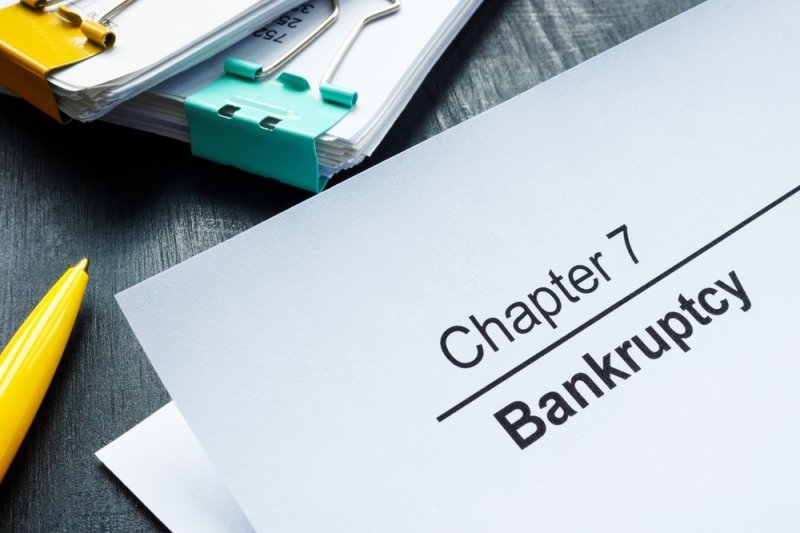 Document labeled “Chapter 7 Bankruptcy” on a desk with paperwork, a clipboard, and a yellow pen.
