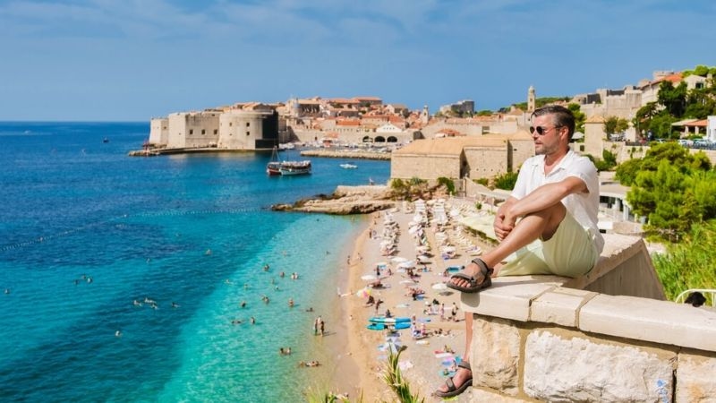 A male traveler enjoys a serene moment by the Adriatic Sea, overlooking the beach of Dubrovnik Croatia