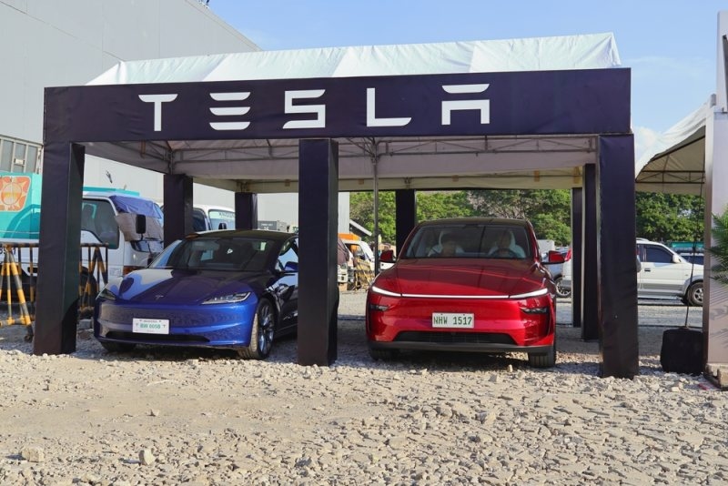 Two Tesla vehicles displayed beneath a Tesla-branded outdoor showroom structure.