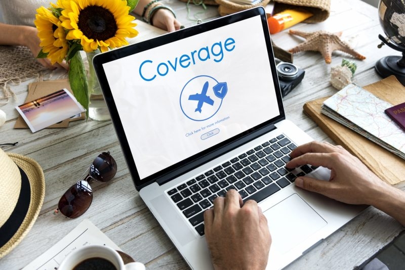Laptop displaying travel insurance coverage information with travel items around it.