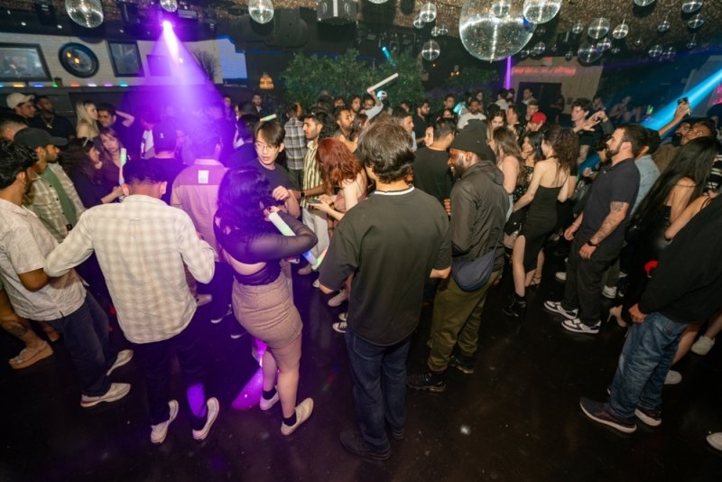 Crowded nightclub with people dancing under colorful lights and disco balls.