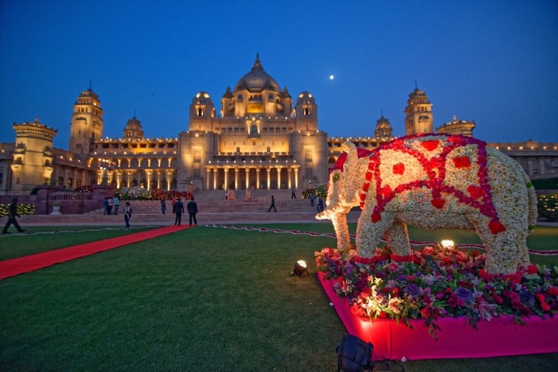 magnificent illuminated palace hotel at dusk, surrounded by landscaped gardens and featuring a large floral elephant sculpture.