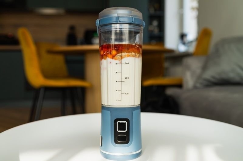 A rechargeable portable blender containing layered ingredients sits on a table.