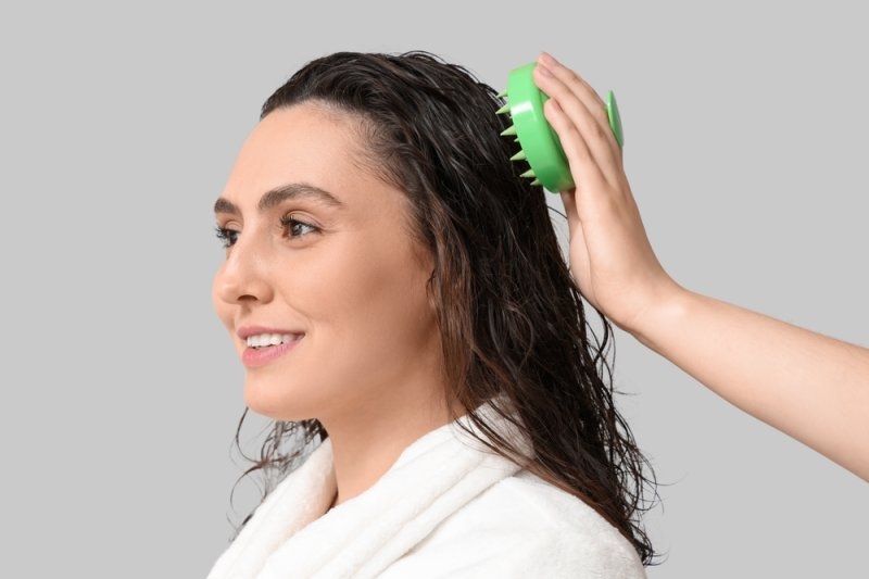Woman using a green scalp massager on her wet hair during a scalp care routine.