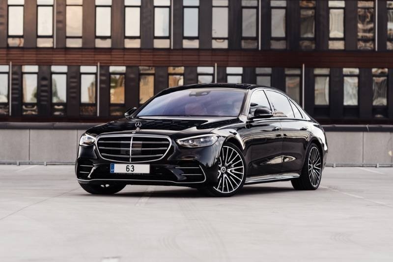 Black luxury sedan parked in front of a modern office building, viewed from the front three-quarter angle.