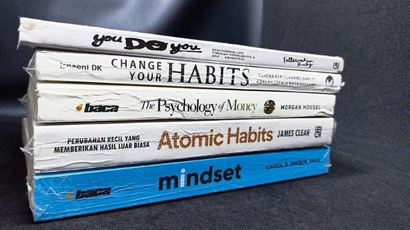 Stack of self-improvement and personal finance books including Atomic Habits, Mindset, and The Psychology of Money.