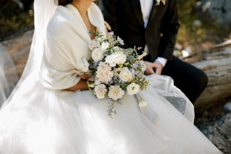 Bride and groom sitting outdoors with the bride holding a white floral wedding bouquet.