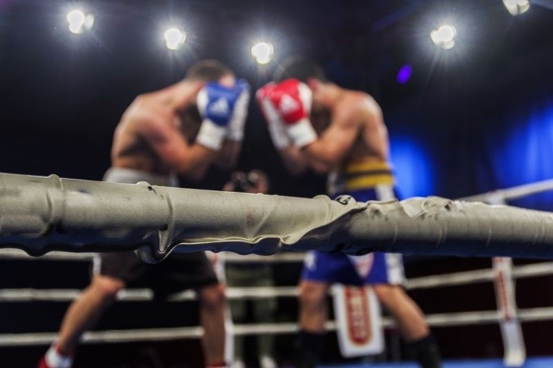 Two boxers sparring in a ring under bright lights, viewed from behind the ropes.