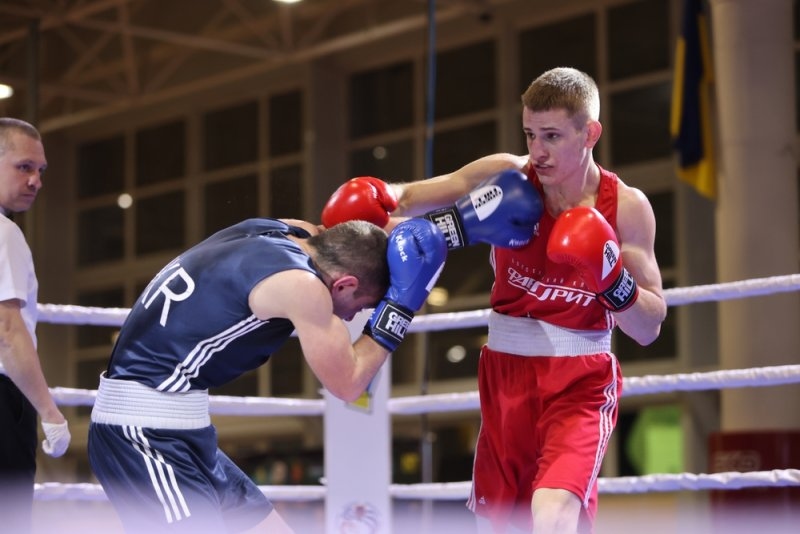 Two boxers competing in a ring, with one boxer in red landing a punch while the other in blue raises his gloves defensively.