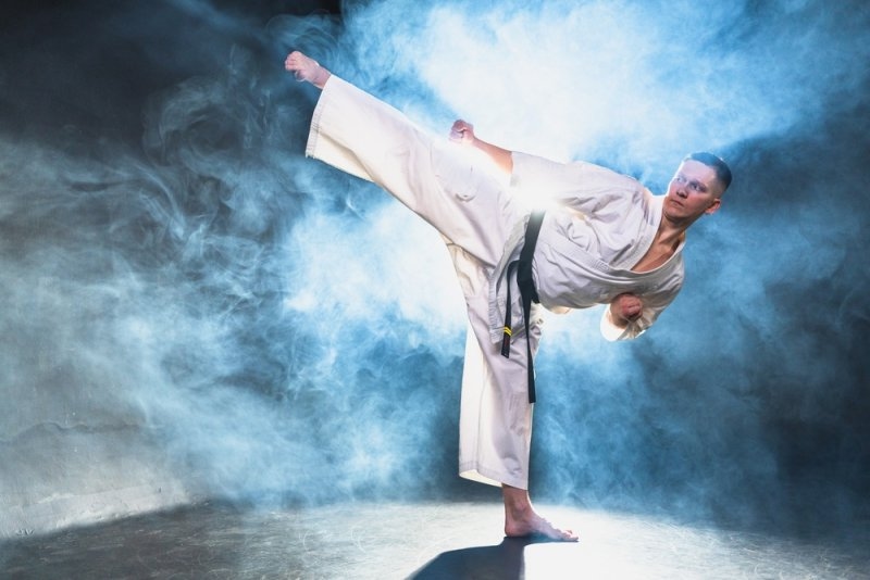 Martial artist in a white uniform performing a high kick against a smoky blue background.
