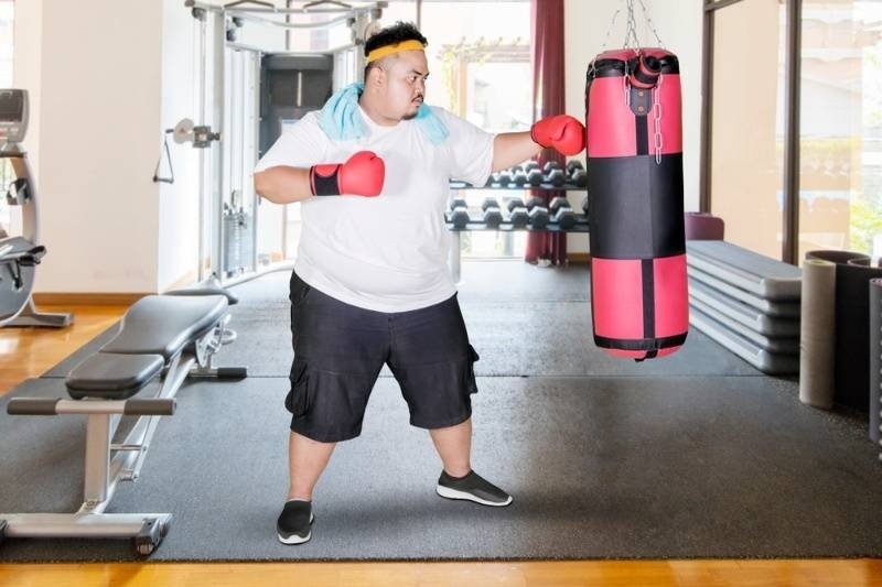 Image of overweight man punching a boxing bag and exercising in the gym center.