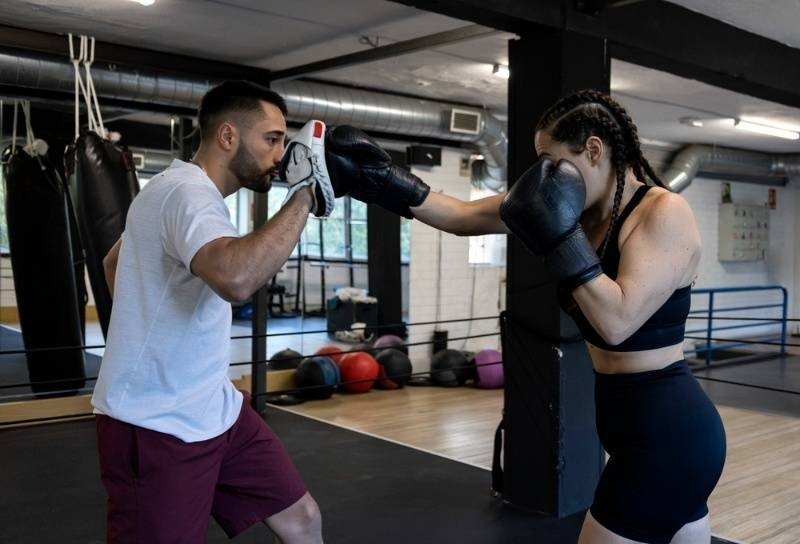 Female boxer sparring with a trainer inside a gym, practicing punching techniques with focus mitts during a boxing workout.