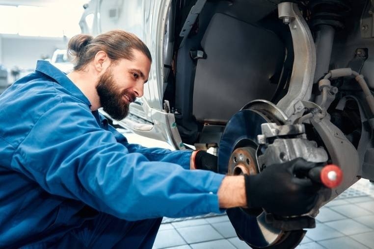 An automotive technician works on a vehicle's exposed brake assembly and wheel hub.