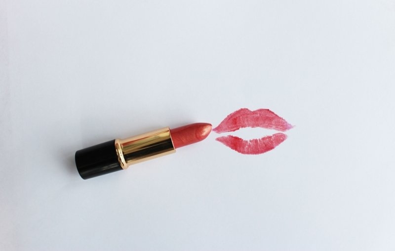 A red lipstick lying on a white surface next to a lipstick kiss imprint.