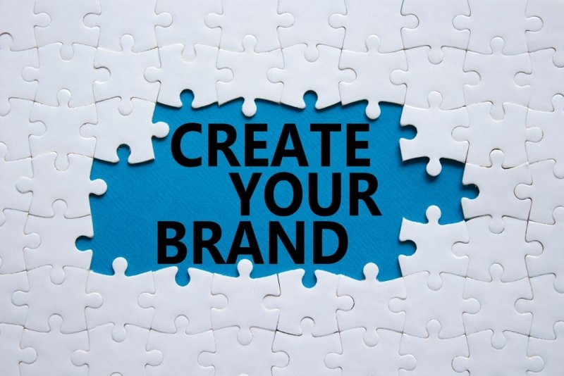 A blue puzzle-shaped space surrounded by white puzzle pieces, featuring the bold message “CREATE YOUR BRAND.”