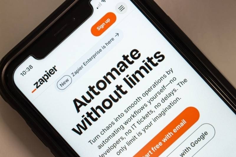 Smartphone displaying Zapier website with 'Automate without limits' message and signup options.