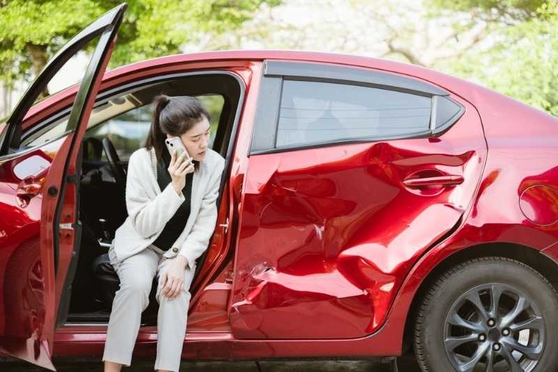 Person sitting in a damaged red car after an accident, talking on the phone.