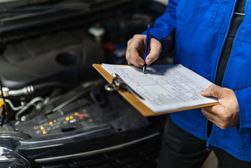 Automotive technician inspecting a vehicle and recording maintenance details.