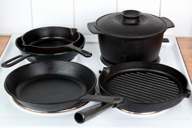 A collection of black cast-iron cookware, including frying pans, a Dutch oven, and a grill pan.