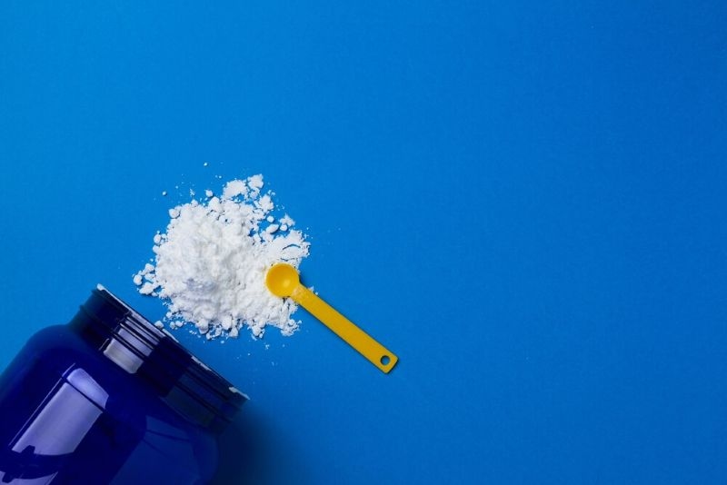 Sports supplement creatine powder on blue background with scoop