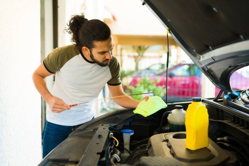 Man checking engine oil levels under the hood of a car with maintenance tools nearby.