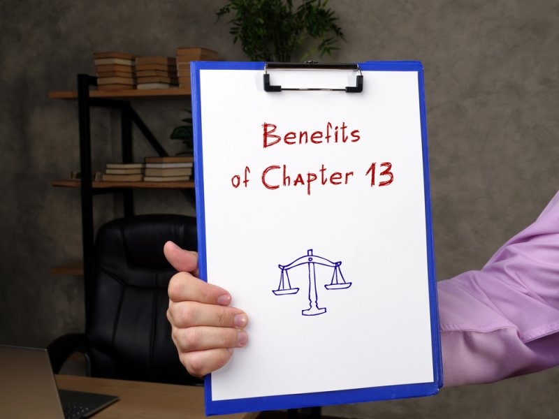 Person holding a clipboard displaying “Benefits of Chapter 13” with a scales of justice illustration.