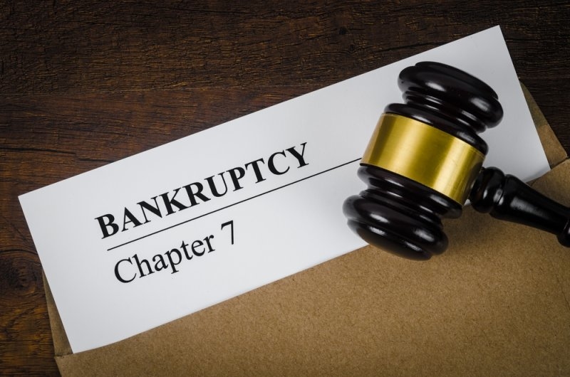 Legal document labeled “Bankruptcy Chapter 7” beside a judge’s gavel on a wooden desk.
