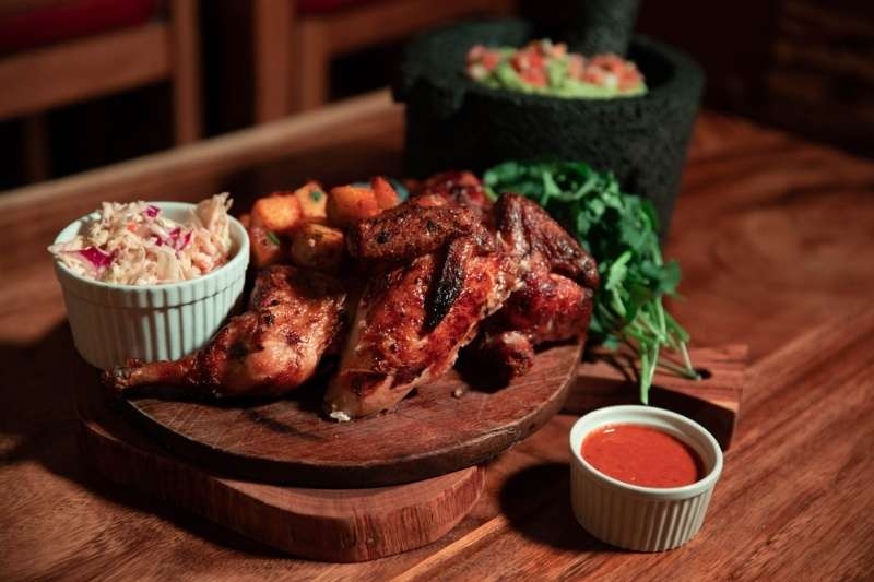 Grilled chicken platter served with sides and dipping sauce on a wooden board.