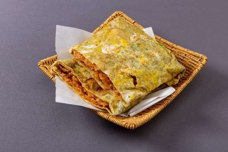 A folded savory crepe or stuffed pancake served in a small woven basket.
