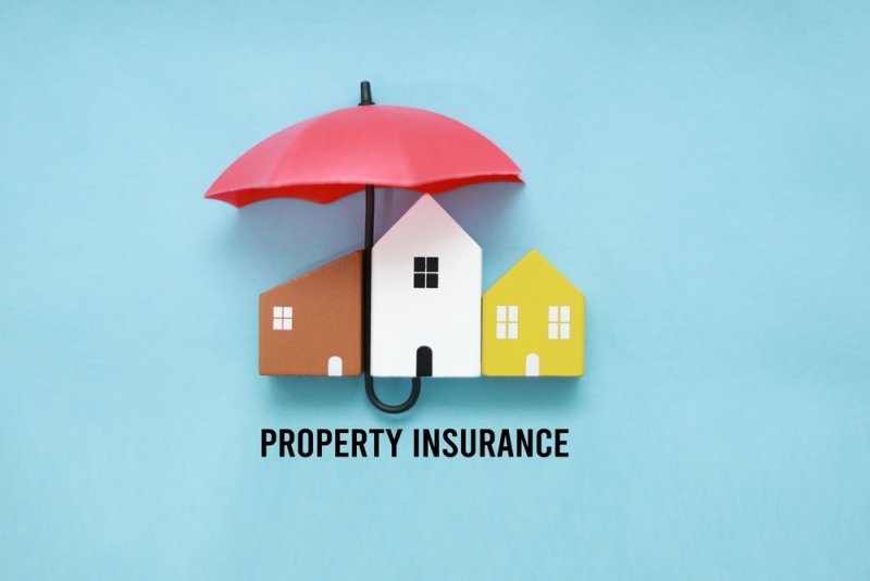 Three model houses sheltered under a red umbrella with the words “PROPERTY INSURANCE” below.