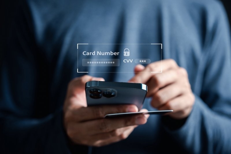 Person using a smartphone with a payment card while a digital overlay displays masked card number and CVV information.